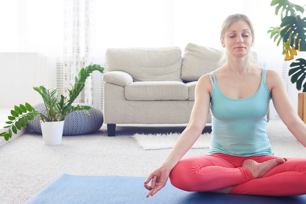 Linda castanha praticando postura de lótus no tapete de ioga interior
 - Foto, Imagem