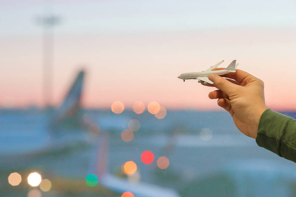 Primer plano mano sosteniendo un avión modelo juguete en aeropuerto fondo ventana grande
 - Foto, Imagen