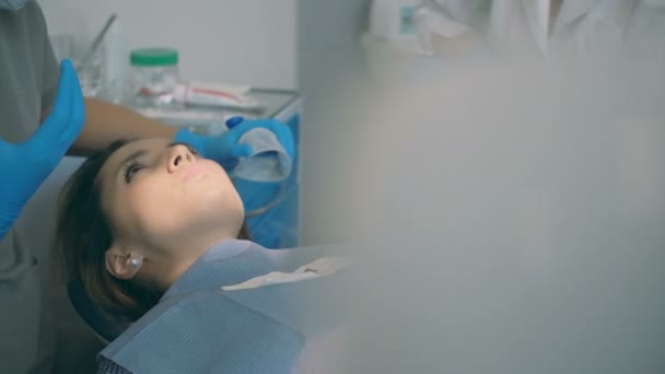 Young woman lying in dental chair and hearing the doctor. Dentist with dental nurse advise the patient. - Filmmaterial, Video