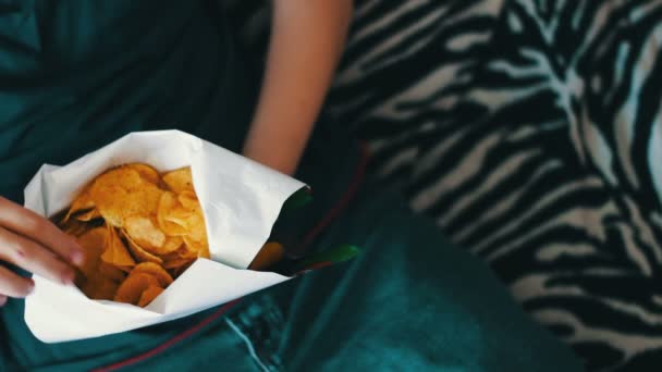 Fiú tinédzser étkezési burgonya chips kezével otthon a kanapén - Felvétel, videó