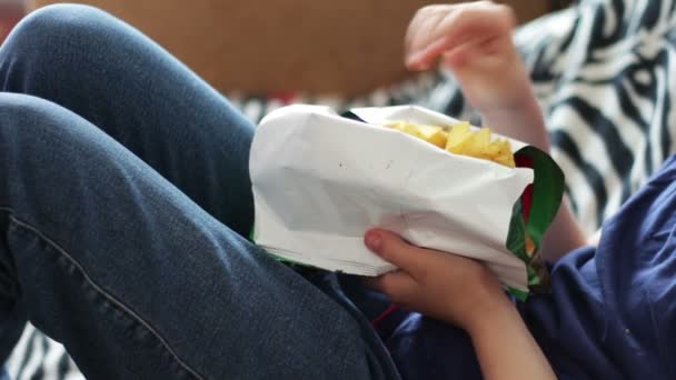 Niño adolescente comiendo papas fritas con las manos en el sofá en home.fast alimentos no saludables
 - Metraje, vídeo