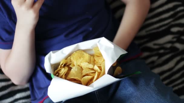 Хлопчик-підліток їсть картопляні чіпси з руками на дивані вдома. швидка їжа нездорова їжа
 - Кадри, відео