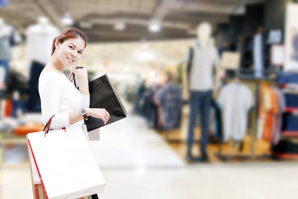 Glück, Konsum, Verkauf und People-Konzept - lächelnde junge Asiatin mit Einkaufstüten über Einkaufszentrum / Suppermarket-Hintergrund - Foto, Bild