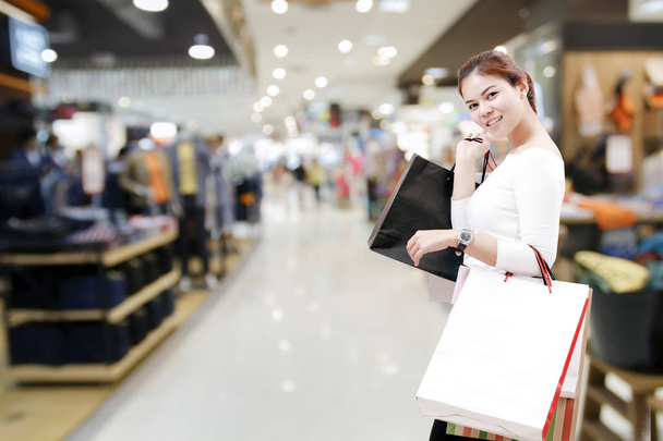 την ευτυχία, τον καταναλωτισμό, πώληση και άνθρωποι έννοια - χαμογελώντας νεαρή γυναίκα Ασίας με σακούλες πέρα από το εμπορικό κέντρο/suppermarket υπόβαθρο - Φωτογραφία, εικόνα