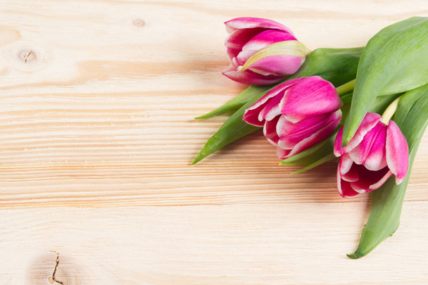 Three pink tulips on a light wooden board - Zdjęcie, obraz