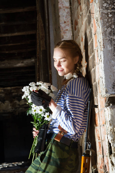 Girl sniper on the ruins with a bouquet of flowers - Фото, изображение