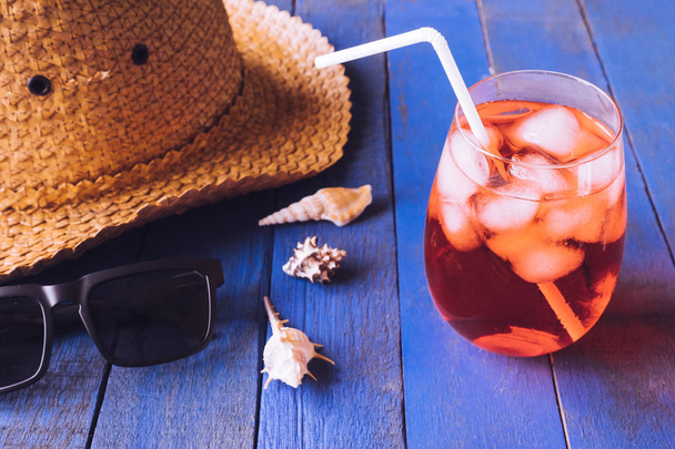 Hut mit Sonnenbrille, rotem Cocktail und Muscheln auf dem Holztisch. Sommerferienkonzept - Foto, Bild