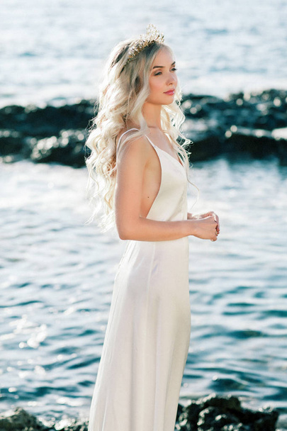 Lovely blond bride in white silk wedding dress posing near the sea - Photo, Image