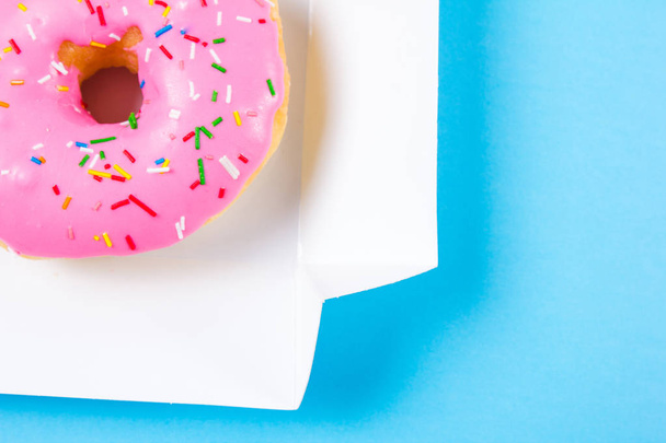 rosafarbener runder Donut in der Schachtel auf blauem Hintergrund. flache Lage, Draufsicht. - Foto, Bild