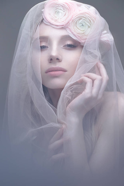 A young girl in the image of a bride with a veil on her face. Beautiful model with a wreath of flowers on her head - Fotografie, Obrázek