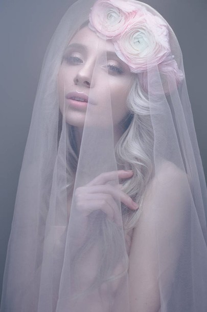 A young girl in the image of a bride with a veil on her face. Beautiful model with a wreath of flowers on her head - Фото, зображення