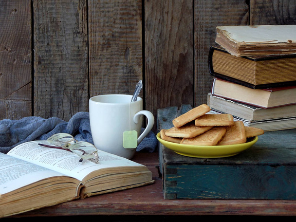 Skład stos starych książek, otwartej książki, filiżanek herbaty, szklanki i talerze cookies cukru na podłoże drewniane. Zdjęcia archiwalne. - Zdjęcie, obraz
