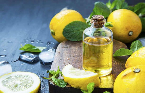Flasche ätherisches Zitronenöl mit Zitronenfrüchten und Minzblättern - Foto, Bild