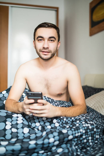 電話アプリを使ったり、ニュース フィードの読み込みで朝ベッドに横たわって髭の男 - 写真・画像