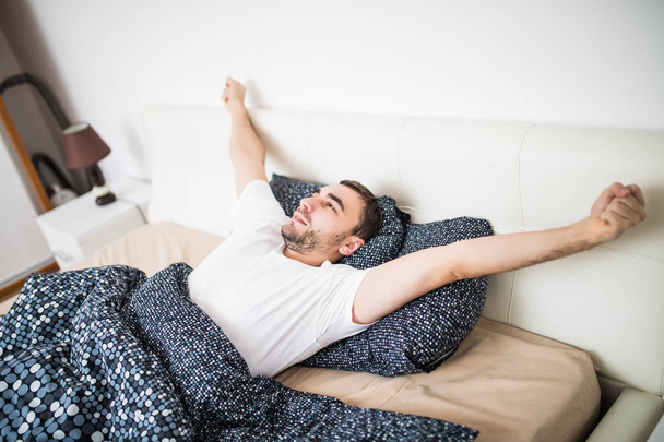 Haukottelu ja venyttely mies herää sängyssä kotona
 - Valokuva, kuva