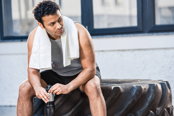 man met fles water rusten op sportschool - Foto, afbeelding