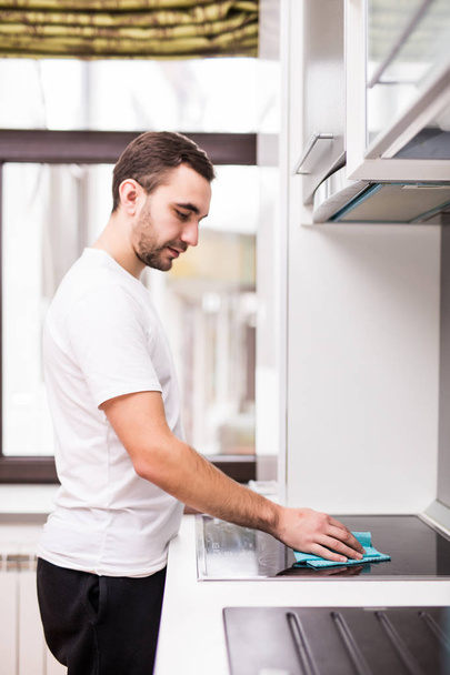Portrait de jeune homme souriant qui nettoie la cuisine dans la maison
 - Photo, image