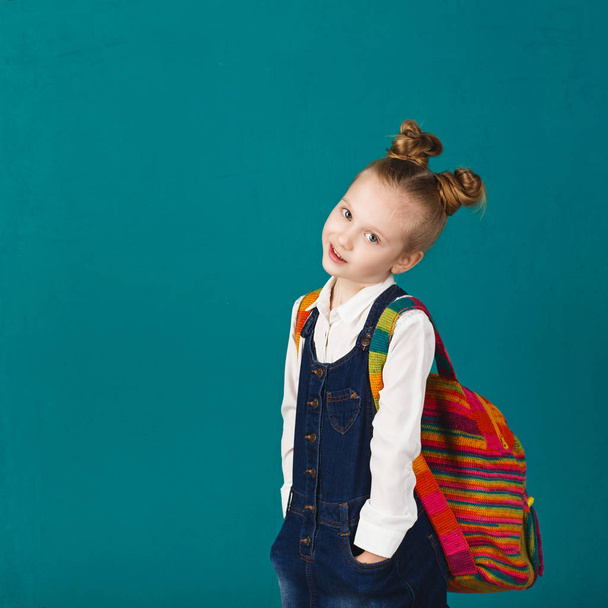 Смешная улыбающаяся маленькая девочка с большим рюкзаком прыгает и имея f
 - Фото, изображение