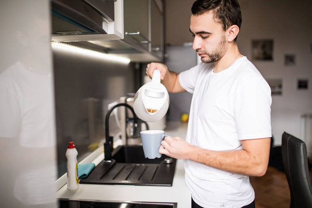 Homem na cozinha derramando uma caneca de café quente de uma panela de vidro. Tomar café da manhã
 - Foto, Imagem
