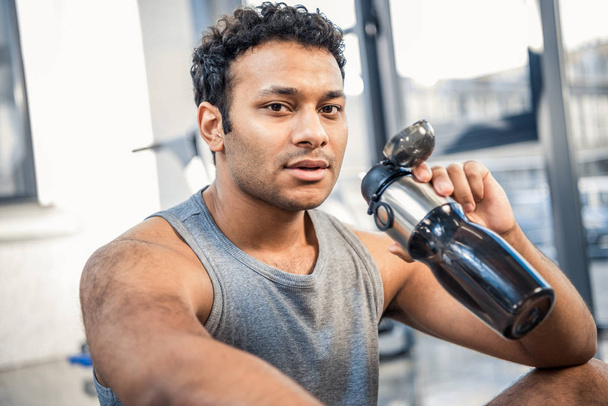 man with bottle of water resting at gym - Photo, Image