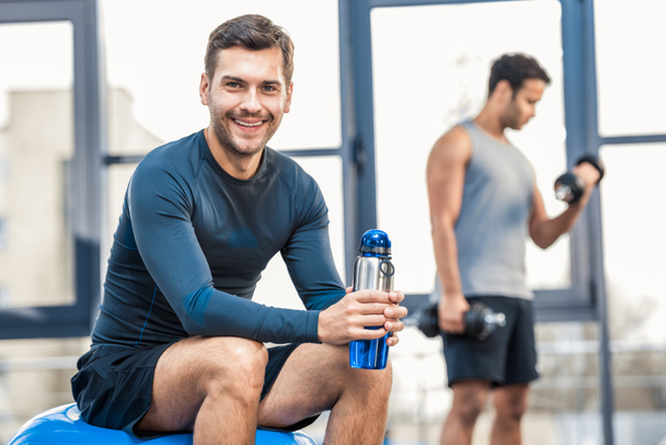 man with bottle of water resting at gym - Photo, Image