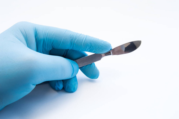 Hand holding scalpel. Palm of surgeon dressed in blue glove holding scalpel. Concept photo for surgeries, procedures, treatment, plastic surgery operation, work of surgical departments and hospitals - Photo, Image