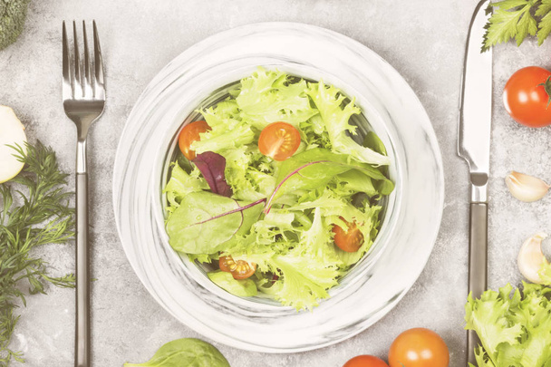 The dietary mixed greens salad (mesclun, mache, lettuce) and cherry tomatoes in a bowl on a light background. Toning - Фото, изображение