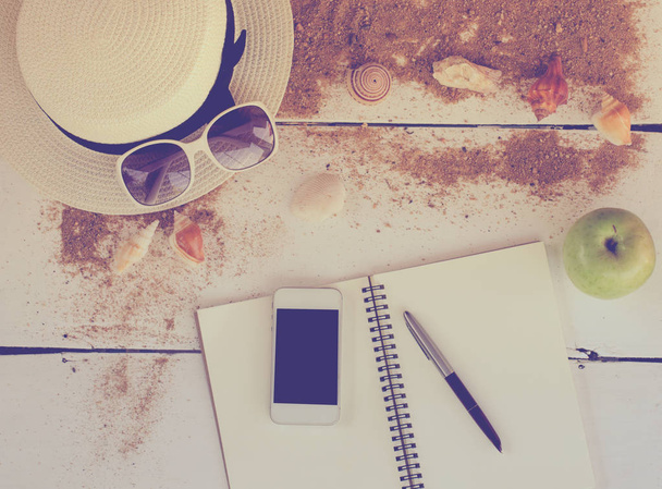 Travel accessories, hats, sunglasses, notebook, pen, phone, shell, placed on a wooden floor - Foto, Imagen