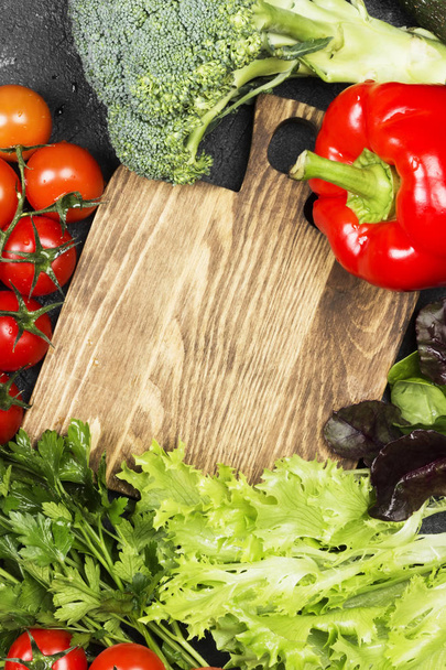 Assortment of fresh vegetables (pepper, cherry tomatoes, onions, garlic, spinach) on a dark background. Wooden cutting board. Top view, copy space. Food background - Φωτογραφία, εικόνα