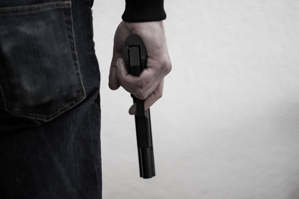 Killer holding a gun to his feet, white background in front of h - Valokuva, kuva