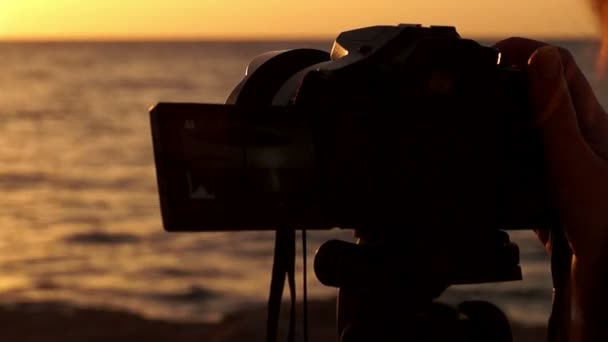 Günbatımında deniz sahilde Tripod üzerinde kamera tutan el. - Video, Çekim