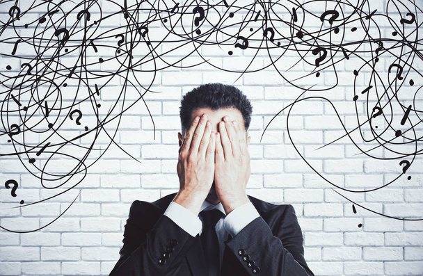 Stressed young businessman with scribble and question marks on white brick background. Confusion concept - Foto, immagini
