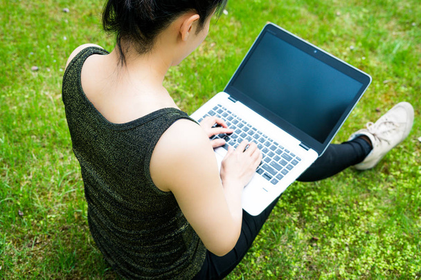 A woman is sitting on the grass while using laptop computer - Foto, Imagen