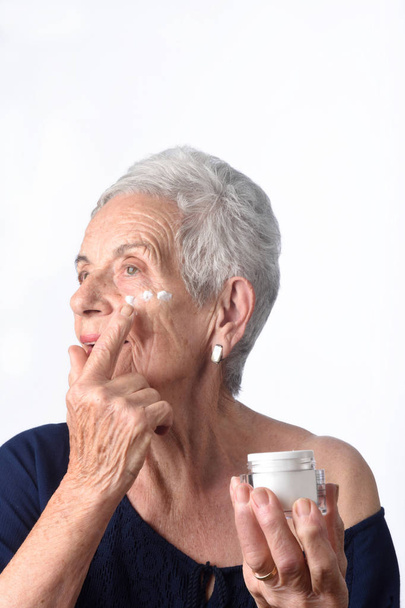 Idősebb nőt alkalmazó krémet vagy hidratáló az arcát - Fotó, kép