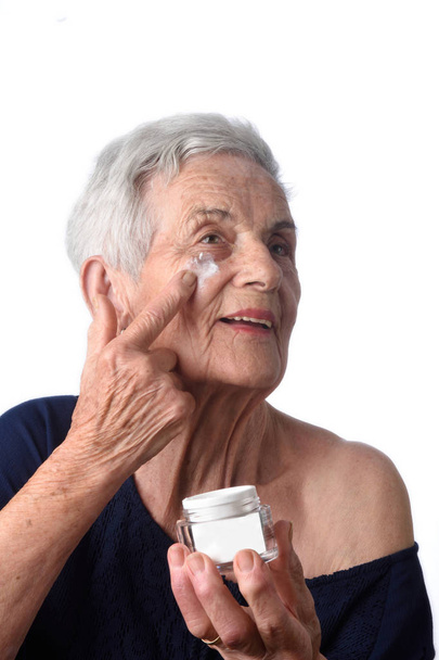 Senior vrouw toepassing huid crème of crème op haar gezicht - Foto, afbeelding
