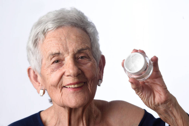 Seniorin trägt Hautcreme oder Feuchtigkeitscreme auf ihr Gesicht - Foto, Bild