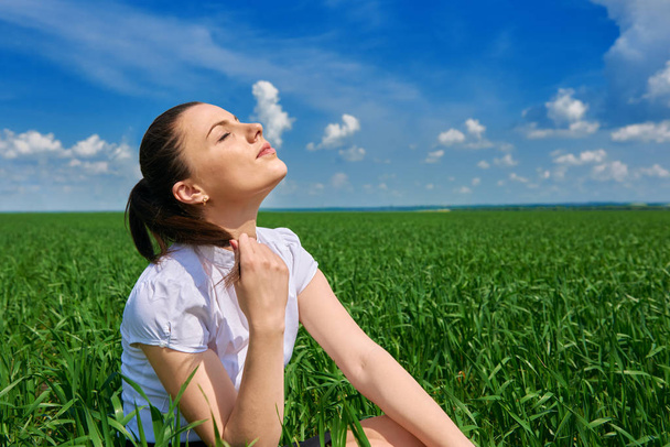 Business woman relaxing in green grass field outdoor under sun. Beautiful young girl dressed in suit resting, spring landscape, bright sunny day - Photo, Image