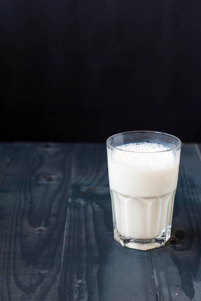 Un vaso de leche sobre un fondo oscuro. Leche en un vaso sobre una mesa de madera
. - Foto, Imagen