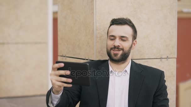 Joven hombre de negocios hablando en la tableta de chat de vídeo con su esposa. Hombre de negocios que utiliza la aplicación para tener una conversación de videoconferencia con su familia durante el descanso
 - Imágenes, Vídeo