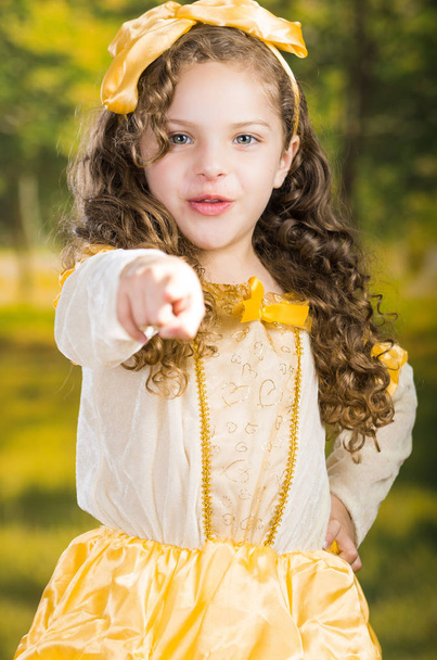 Cute little girl wearing beautiful yellow dress with matching head band, posing for camera, green forest background - Фото, зображення