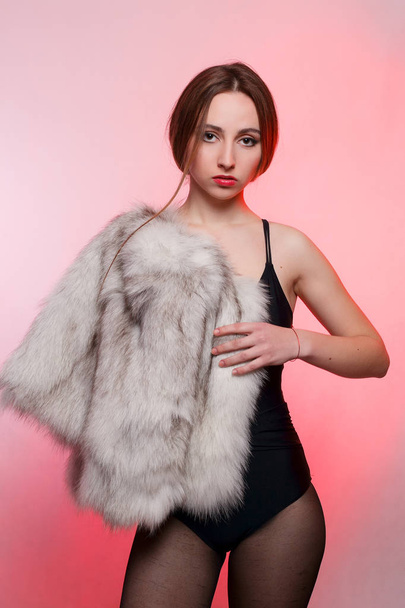 Fashionable beautiful woman in a gray fur coat of artificial fur on a red background stands frowning - Foto, imagen