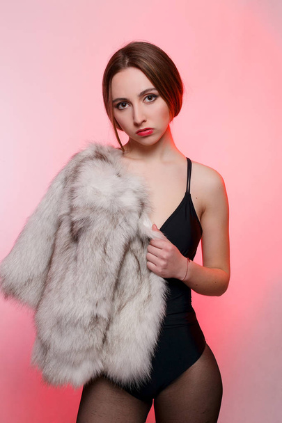 Fashionable beautiful woman in a gray fur coat of artificial fur on a red background stands frowning - Photo, Image