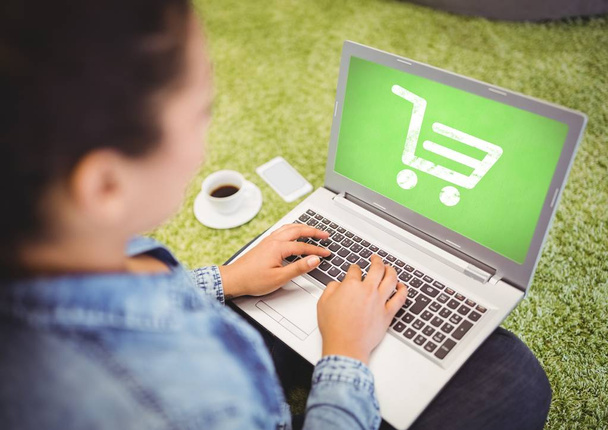 Woman using laptop with Shopping trolley icon - Фото, изображение