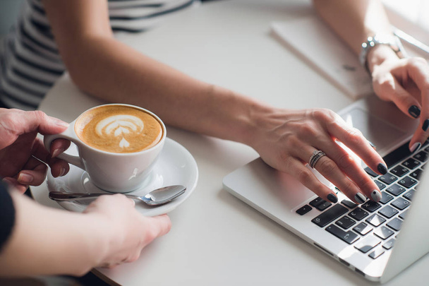 Close-up foto van handen van een ober die een kopje cuppuccino om een vrouw te typen met een toetsenbord. - Foto, afbeelding