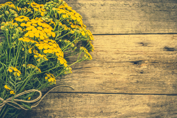 Yellow flowers from summer meadow, rustic bouquet located on wooden background - Foto, afbeelding
