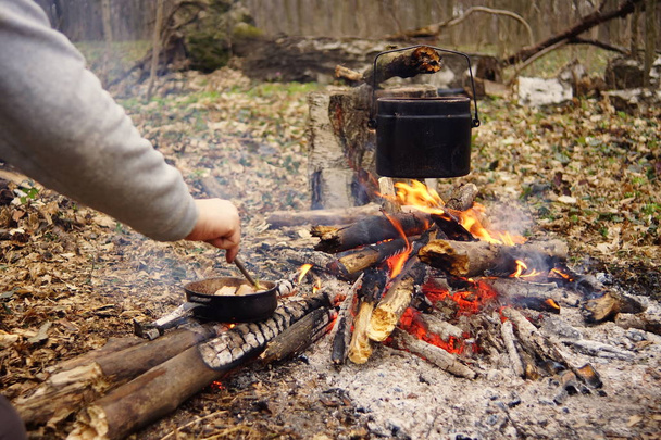 Wasserkocher am Lagerfeuer mit Zelt im Hintergrund. Hand mit Stock über Feuer - Foto, Bild