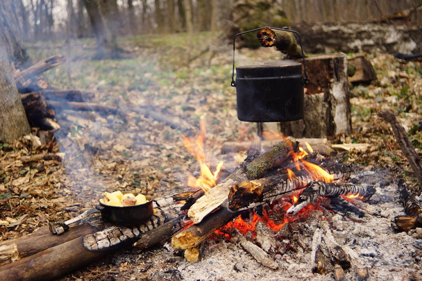 Wasserkocher am Lagerfeuer mit Zelt im Hintergrund. Hand mit Stock über Feuer - Foto, Bild