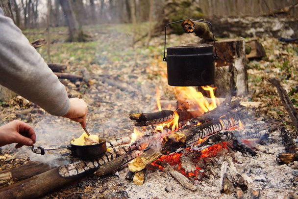 として野生のキャンプで焚き火の上に食べ物を準備します。 - 写真・画像