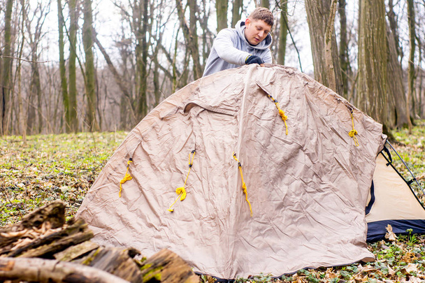 Young man putting a tent in the woods a - 写真・画像