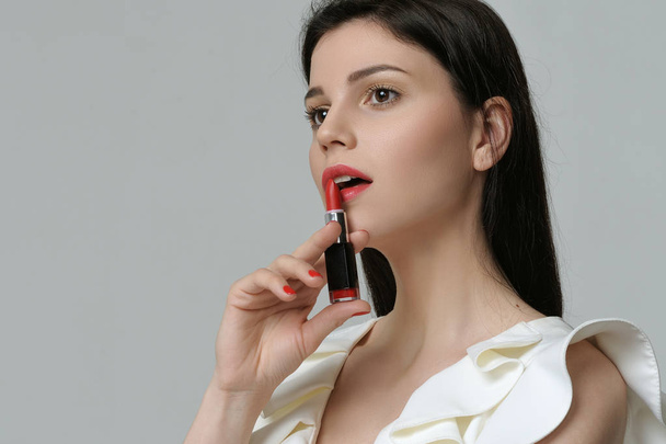Portrait of a cute girl who holds a lipstick near her lips like  - Valokuva, kuva